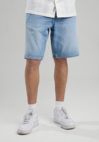 Light blue denim shorts with a relaxed fit, side pockets, and frayed hem, paired with white sneakers and ankle socks.