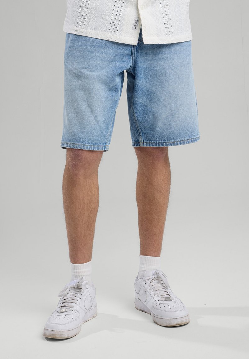 Light blue denim shorts with a relaxed fit, side pockets, and frayed hem, paired with white sneakers and ankle socks.