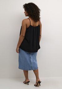 Top nero senza maniche con schiena arricciata, abbinato a una gonna di jeans a media lunghezza. Presenta spalline sottili e una vestibilità rilassata. Sandali neri con tacco.