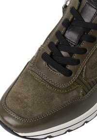 Sneaker verde oliva con lacci neri, pannelli in suede e pelle, cuciture dettagliate e suola in gomma bianca con accenti neri sulla suola.