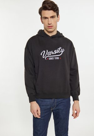Fekete kapucnis pulóver, fehér hímzett "Varsity" és "SINCE 1998" szöveggel, piros csillagokkal díszítve, puha anyagból készült, laza szabással.