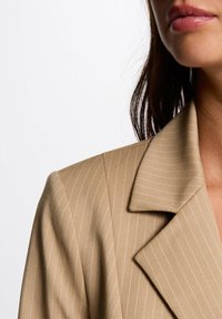 Beige gestreepte blazer met een geknipt kraag en een gladde textuur, met zichtbare stiksels langs de randen.