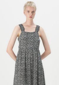 Μαύρο και λευκό φόρεμα με λουλουδάτο σχέδιο, τετράγωνη λαιμόκοψη, υφασμάτινες τιράντες και φουσκωτή, συλλεγμένη φούστα. Λείο ύφασμα, casual σχεδίαση.