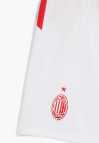 Pantalones cortos deportivos blancos con rayas laterales rojas, que presentan el logo en rojo y blanco del AC Milan con una estrella encima.