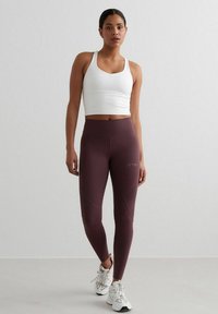 White sports bra paired with high-waisted, maroon leggings featuring dynamic seam design. Model wears white athletic shoes.