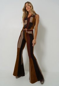 Two-piece outfit made of corduroy featuring a cropped vest and flared pants. Color palette includes brown, tan, and dark brown with patchwork design.