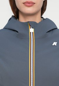 Gray hooded jacket with a front zipper, featuring a multi-color trim and a logo on the chest. Smooth material with a fitted design.