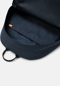 Tmavě modrý batoh se zipovým uzávěrem, který má prostorný vnitřní prostor a vnitřní kapsu. Vyroben z odolné tkaniny s texturovaným povrchem.