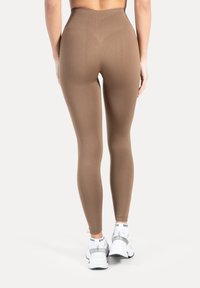 Leggings marron taille haute en matière extensible, avec une texture lisse et une coupe ajustée. Des baskets blanches avec des accents gris sont portées.