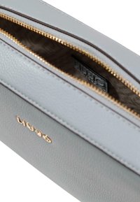 Grå læderpose med gyldent lynlås, der har et mønstret indvendigt for og et mærkelogo præget på ydersiden.