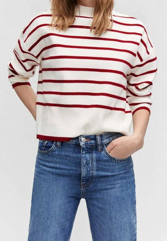 Pull en maille blanche avec des rayures horizontales rouges, doté d'un col montant et d'une coupe décontractée. Associé à un jean bleu taille haute, affichant un look décontracté.