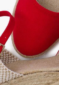 Espadrilles de lona roja con suela de yute trenzado. Presentan una punta redonda y plana, y una correa para el tobillo a juego en rojo, mostrando materiales texturizados.