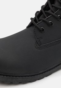 Black waterproof ankle boot with a smooth synthetic upper, lace-up design, reinforced toe, and textured rubber sole for traction.
