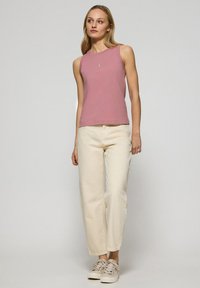 Różowa bawełniana bluzka bez rękawów z okrągłym dekoltem, zestawiona z kremowymi spodniami o szerokich nogawkach i beżowymi trampkami. Prosty detal logo na bluzce.