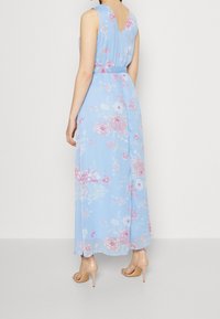 Lång blå blommig klänning med V-ryggdesign, prydd med pastellrosa och vita blommönster. Lättviktig tyg och figurnära midjedetalj.