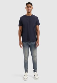 Navyblauw T-shirt met korte mouwen en ronde hals, gecombineerd met lichtblauwe slim-fit jeans en witte sneakers met zwarte accenten.