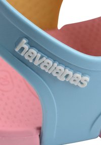 Sininen kuminen liukuestekenkä, jossa on teksturoitu vaaleanpunainen pohja; varressa korotettu valkoinen "havaianas"-logo.