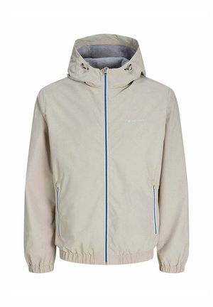 Veste à capuche beige clair avec fermeture éclair frontale accentuée de bleu, poches latérales zippées, poignets élastiques et logo "originals stripe" sur la poitrine.