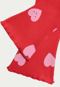 Røde ribbede stof benvarmere med store lyserøde hjerter med smilende ansigtstræk. Tekstureret finish med en bølget kant langs kanterne.
