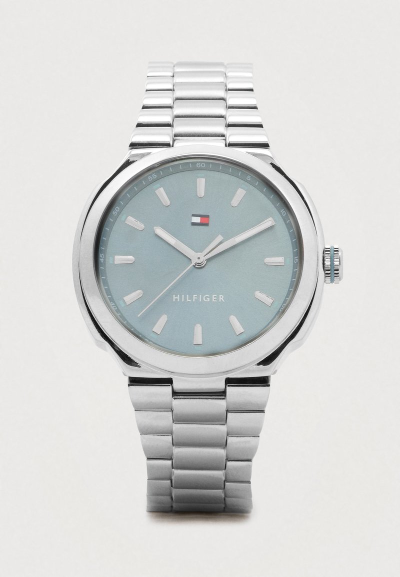 Silver metal wristwatch with blue face, white hour markers, three hands, and Tommy Hilfiger logo and brand name on the dial.