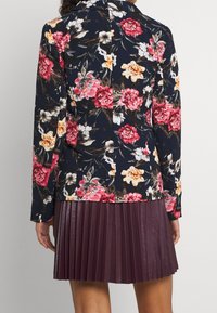 Květinová košile s dlouhým rukávem v námořnické modři s živými růžovými, oranžovými a bílými květy. Kombinováno s plisovanou burgundskou sukní z umělé kůže.