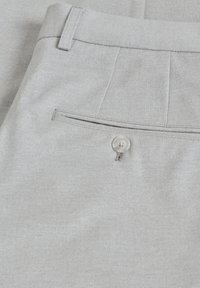 Pantalons gris clair avec une texture lisse, comportant une poche arrière fermée par un bouton et un design épuré et ajusté.