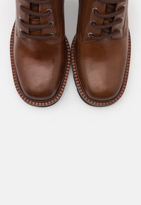 Bottines en cuir marron avec bouts ronds, dotées de lacets marron texturés, d'œillets en métal et d'une semelle en caoutchouc striée.