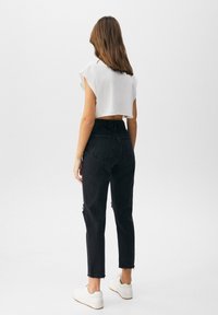Top corto blanco con mangas cortas, combinado con jeans negros de talle alto que tienen bordes deshilachados y un detalle desgastado, usado con zapatillas blancas.