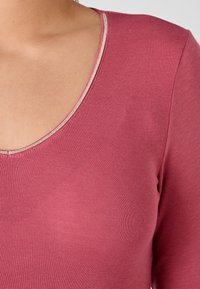 Maglia a maniche lunghe in morbido tessuto a costine rosa chiaro, con scollatura arrotondata e un dettaglio metallico intorno al collo.