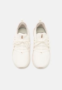 White athletic shoes with a textured mesh upper, thin laces, and a subtle golden logo on the tongue. Rounded toe and cushioned sole.