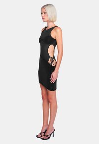 Schwarzes ärmelloses Kleid mit Ausschnitten, Bindebändern an den Seiten und einer enganliegenden Silhouette. Glattes Gewebe mit leichtem Glanz. Minimalistisches Design.