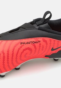 Črne nogometne klice z živahnim rdečim dizajnom in teksturiranim vzorcem, označene z "PHANTOM GX," ter zanko za lažje obuvanje.