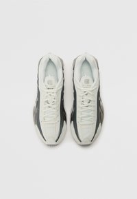 Witte en zwarte atletiekschoenen met een gestructureerde bovenkant, gladde afwerking en een opvallend vetersysteem. Voorzien van een gevoerde binnenkant en een slank ontwerp.