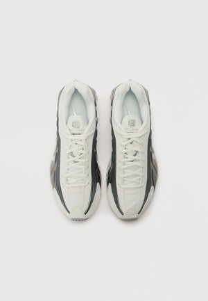 Vita och svarta atletiska sneakers med en texturerad ovandel, slät yta och framträdande snörningssystem. Utrustade med ett vadderat innerskikt och en stilren design.