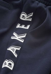 Marinblå joggingbyxor i ett strukturerat tyg, med djärva vita bokstäver "BAKER" längs sidan. Elastisk midja och små fickdetaljer.