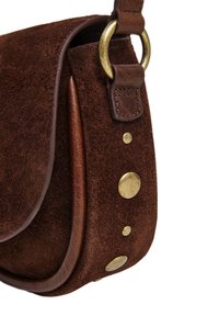 Smeđa suede torba preko tijela s zakrivljenim preklopom, kožnom trakom i brass hardverom koji uključuje studove i prsten, ističući teksturu i dizajn.