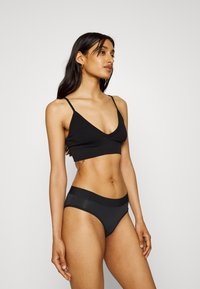 Zwarte ribbelige bralette met dunne bandjes en een diepe V-hals, gecombineerd met lage zwarte ondergoed met een contrasterende tailleband.