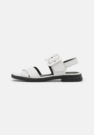 White leather sandals with a wide strap, adjustable buckle closure, open toe design, and black rubber sole for traction.