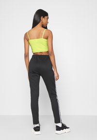 Svarta joggers med vita sidosträck, i kombination med en ljusgrön cropped top med tunna axelremmar. Slät tygstruktur synlig.