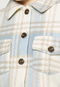 Flanellen overhemd met een blauw, beige en witte ruitpatroon, plastic knopen en twee borstzakken. Zachte textuur met een kraagontwerp.