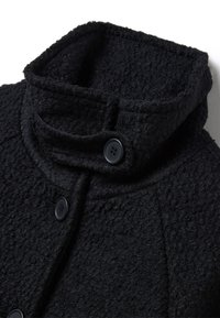 Cappotto nero texturizzato con colletto alto e due chiusure a bottone. Il tessuto sembra morbido con una finitura leggermente pelosa.