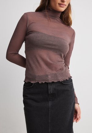 Woman wearing a fitted, long-sleeve, semi-sheer brown top with lettuce hem paired with a high-waisted black denim skirt.