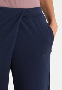 Pantalons de sport bleu marine avec une texture douce, ornés d'un logo Nike noir, d'une poche zippée et d'un design de ceinture croisée.