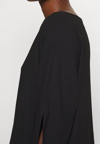 Czarna bluzka z luźnym krojem, z szerokimi rękawami i bocznymi rozcięciami, gładka w dotyku, minimalistyczny design oraz okrągły dekolt.