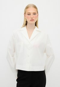 White cropped button-up shirt with a pointed collar, single chest pocket, and slightly relaxed fit. Smooth, lightweight fabric.