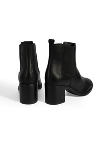 Bottines en cuir noir avec des panneaux latéraux élastiques et un talon bloc. Texture lisse avec un bout arrondi et des détails de design minimalistes.