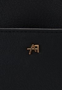 Černá texturovaná kůže se zlatým kovovým logem s písmeny 'AF' v moderním fontu, s viditelnými prošitými okraji nahoře.