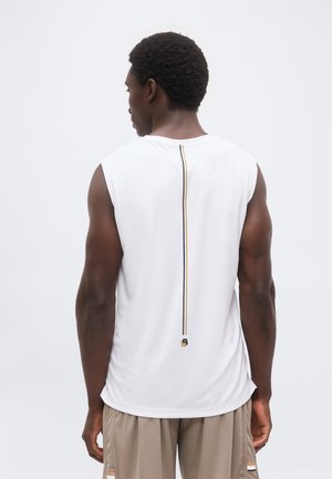 Man met een donkere huid en kort krullend haar, die een mouwloos wit shirt draagt met een verticale zwarte en beige streep midden op de rug, beige korte broek.