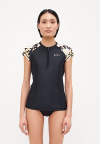 Black short-sleeve rash guard with floral-patterned sleeves, zipper front, and BILLA BONG logo. Made from stretchy, quick-drying material.