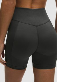 Aukštai liemeniai juodi sportiniai šortai, pagaminti iš lygios, elastingos medžiagos su tekstūruotomis šoninėmis dalimis ir plokščiais siūlais, užtikrinančiais komfortą ir paramą.